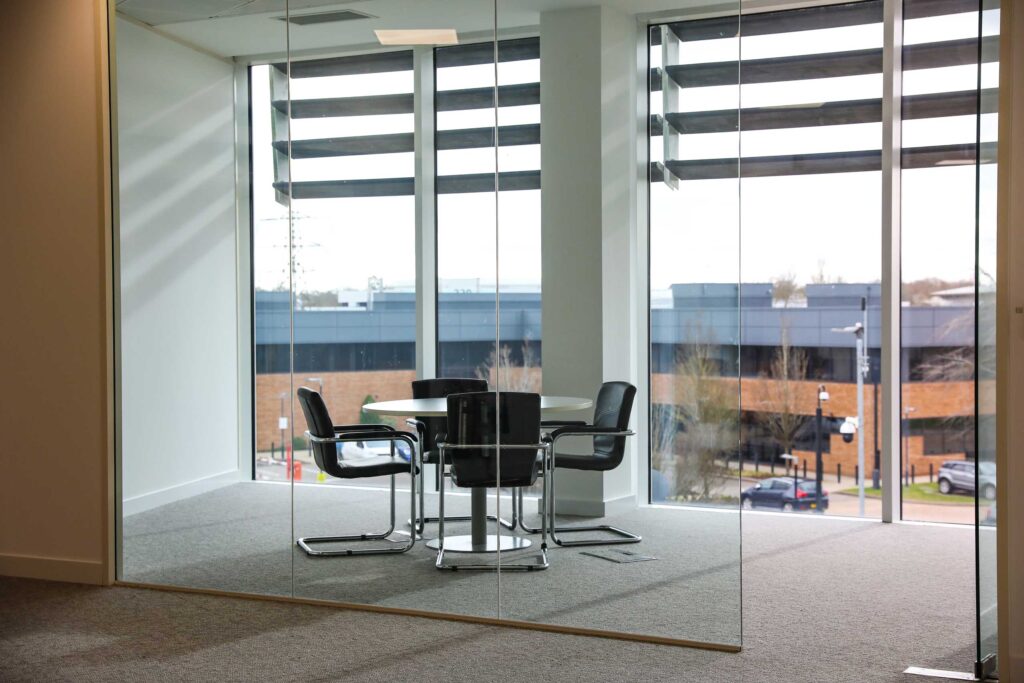 A glass walled office with a table and chairs.